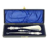 A cased set comprising silver handled button hooks and shoe horn with cherub decoration.
