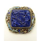 A silver gilt brooch with enamel decoration and central carved lapis lazuli panel.