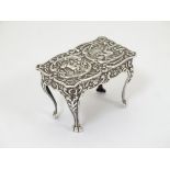 Silver dolls house furniture : A miniature silver table with floral scroll and cherub decoration on