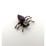 A small charm formed as an insect with amethyst coloured body and white stone head.
