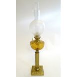 An oil lamp with brass square base supporting a column stand and dimpled orange glass reservoir.