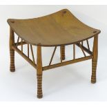 An early 20thC oak Liberty style Thebes stool with a concave seat above brace supports and turned