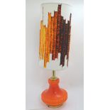 A vintage retro table lamp, with neon orange glass base and printed fabric shade,