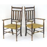 A pair of Arts and Crafts open armchairs with slatted backrests and swept arms above envelope rush
