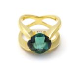 A gold ring set with central green tourmaline flanked by 2 diamonds.