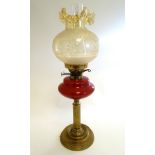 An oil lamp with brass base supporting a column stand and red glass reservoir,