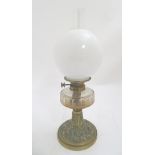 A Victorian oil lamp with a brass base decorated with cast foliate detail,