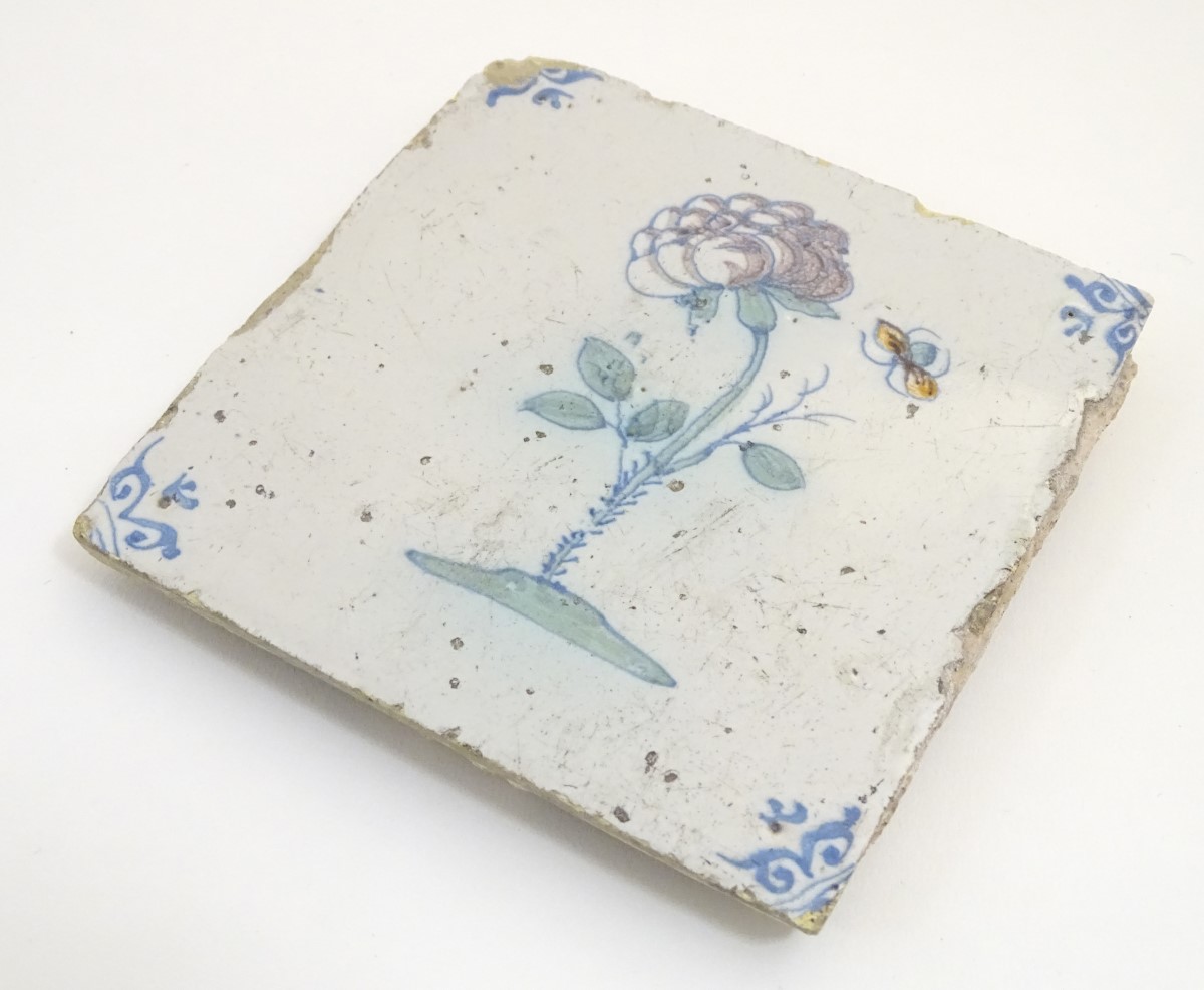 A 17thC Delft tile depicting a flower and a flying insect, with blue ox-head corner motifs. Approx.