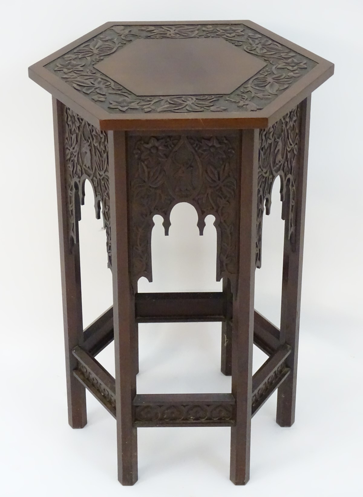 A walnut Liberty style table with a hexagonal carved top above six matching carved facades with