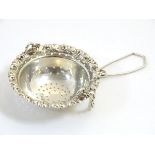 A silver tea strainer with spout hanging attachment.