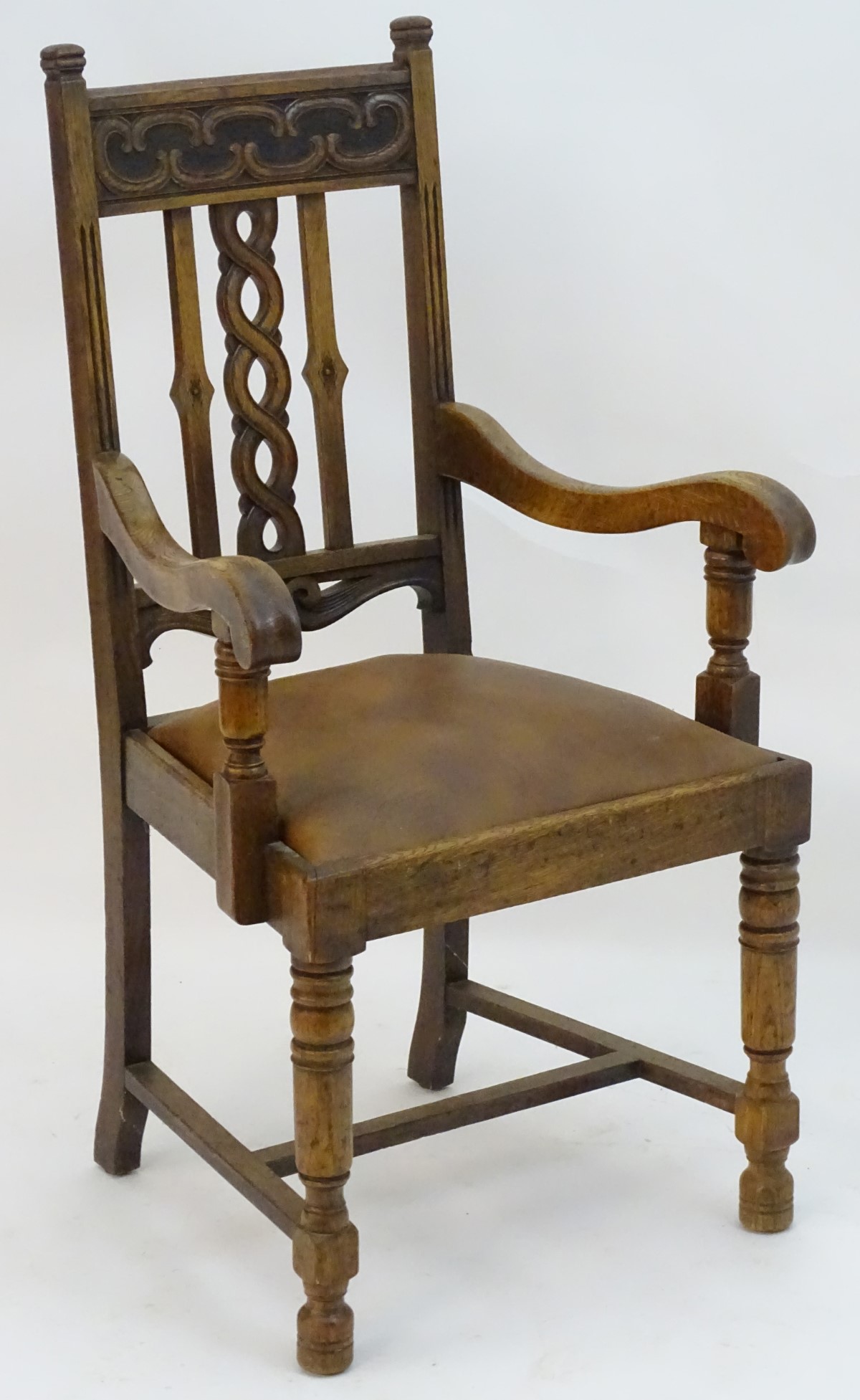 An early 20thC oak open armchair with a Celtic style carved top rail and back ress,