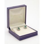 A pair of 9ct white gold stud earrings set with central emerald bordered by diamonds in a cluster