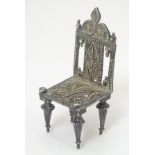A silver miniature model of a chair with filigree decoration.