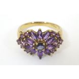 A 9ct gold dress ring set with a profusion of amethysts with a central blue stone.