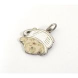 A mid 20thC novelty white metal pendant charm formed as a humorous face wearing a chamber pot as a