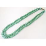 A vintage two-strand bead necklace if graduated jade green coloured beads with a silver gilt clasp.