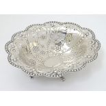 A silver dish with punch, pierced and embossed decoration and standing on four feet.