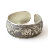 An Art Deco white metal bangle formed bracelet with elephant decoration .