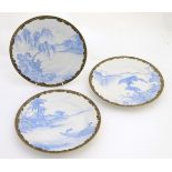 Three Japanese blue and white plates with landscape views and gilt patterned borders,