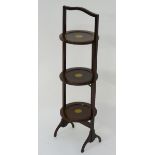 An early 20thC mahogany folding cake stand with three marquetry decorated tiers.