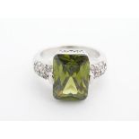 A 14kt white gold ring set with central peridot flanked by diamonds to the shoulders. The central