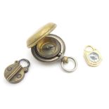 A cased pocket compass, together with a pendant/charm compass in yellow metal mount and a small