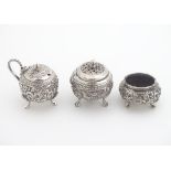 Assorted white metal cruet items comprising mustard pot, pepper and salt. with various decoration.