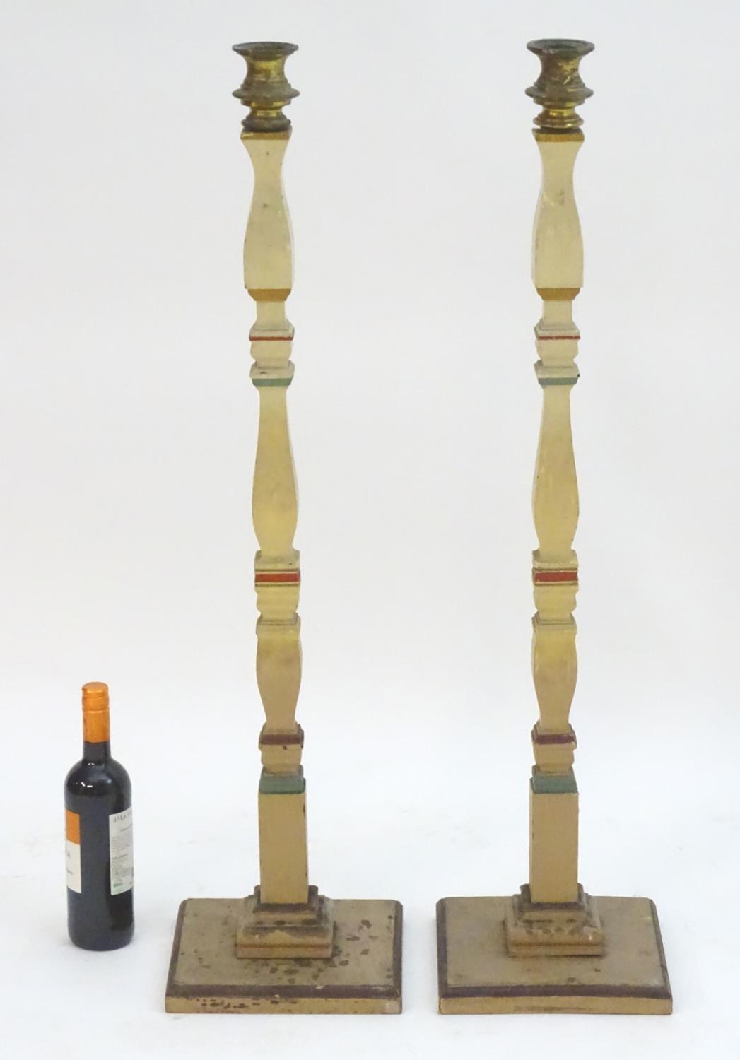 A pair of 20thC tall squared based candlesticks of carved wooden form with painted decoration and