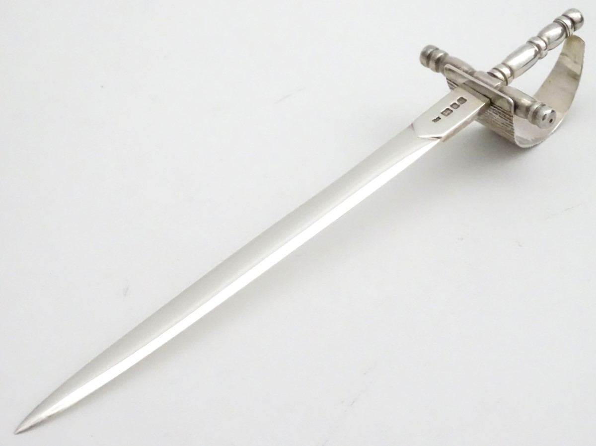 A silver novelty silver paper knife in the form of a basket hilt rapier sword. Hallmarked