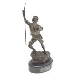 A 20thC bronze depicting a hiking boy scout standing atop a rocky outcrop. Raised on an oval