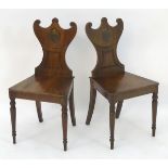 A pair of mahogany Regency hall chairs with shaped and carved backrests above turned tapering