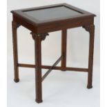 A mahogany bijouterie table with a glass top, carved earpieces and legs united by a cross stretcher.