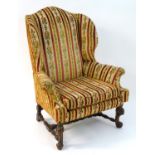 An early 20thC wingback armchair standing on carved scrolling front legs uniting the back legs