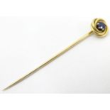 A 14ct gold stick pin surmounted by yellow metal knot decoration set with blue stone to centre.
