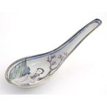 A Chinese famille rose soup spoon decorated with a figure in a landscape with a cherry blossom tree.