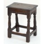 A late 17thC oak joint stool with a rectangular top, carved apron and standing on cannon barrel