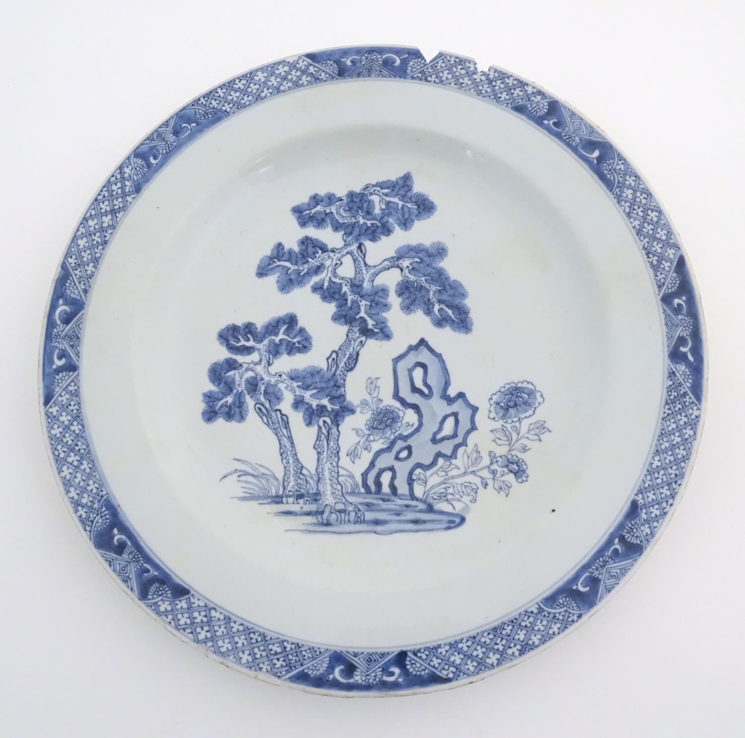 A Chinese blue and white charger decorated with a stylised landscape with trees and flowers, and a