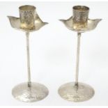 A pair of silver candlesticks in the Arts & Crafts style with hammered decoration and flower