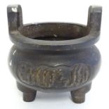 A Chinese cast bronze three footed censer with script decoration and upright twin handles. Character