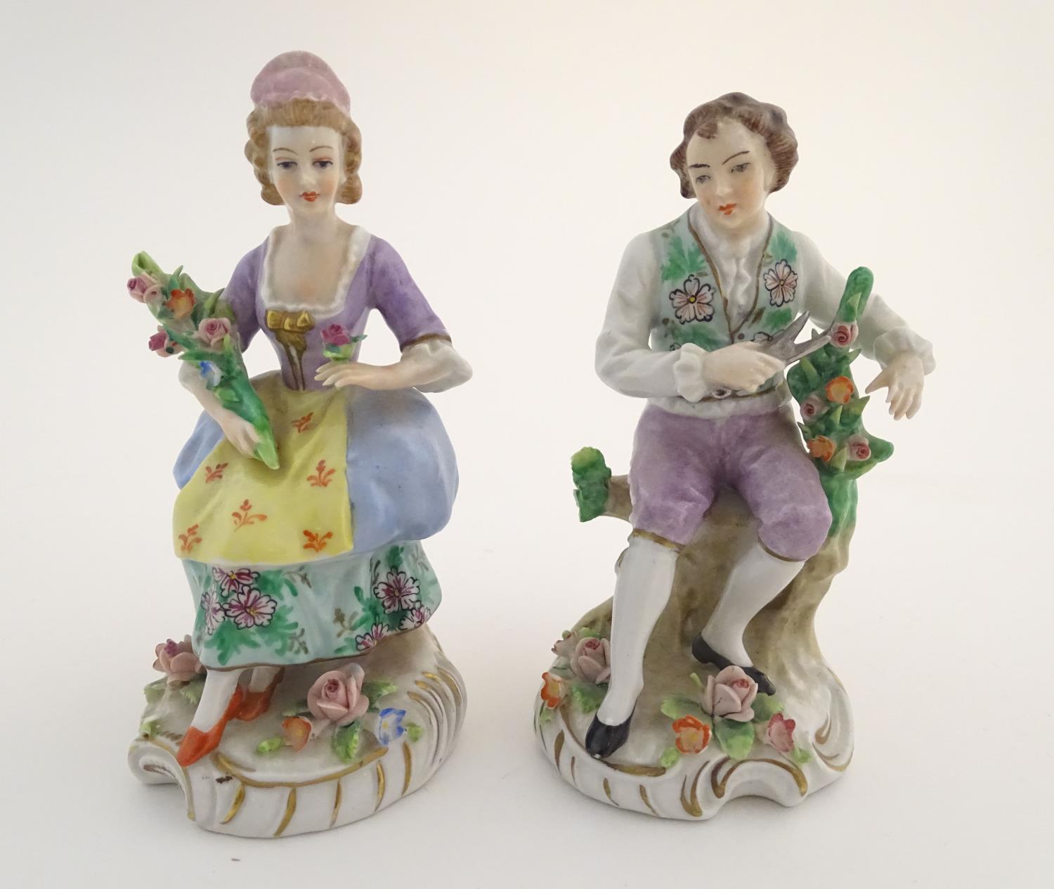 A pair of German Sitzendorf porcelain florist figures, a gentleman and lady, each seated on a