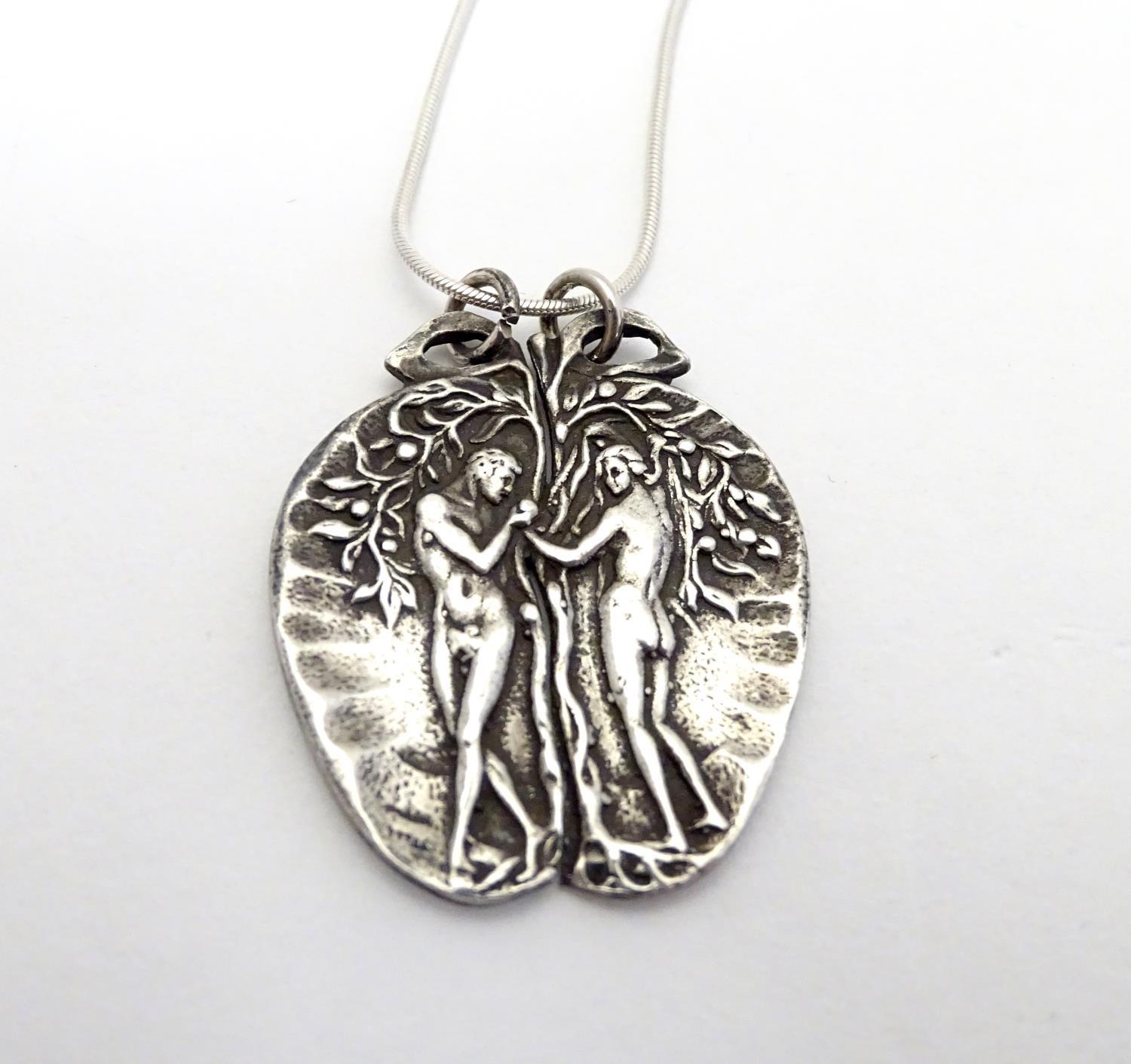 A silver pendant on chain, the pendant formed as an apple with a depiction of Adam and Eve.