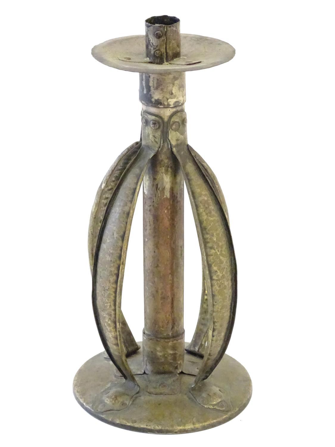 An Arts and Crafts copper and brass candlestick with a hammered finish and bowed strapwork supports,