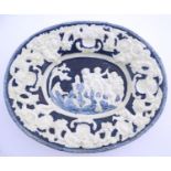 An Italian style charger of oval form with relief decoration depicting putti in a landscape. The