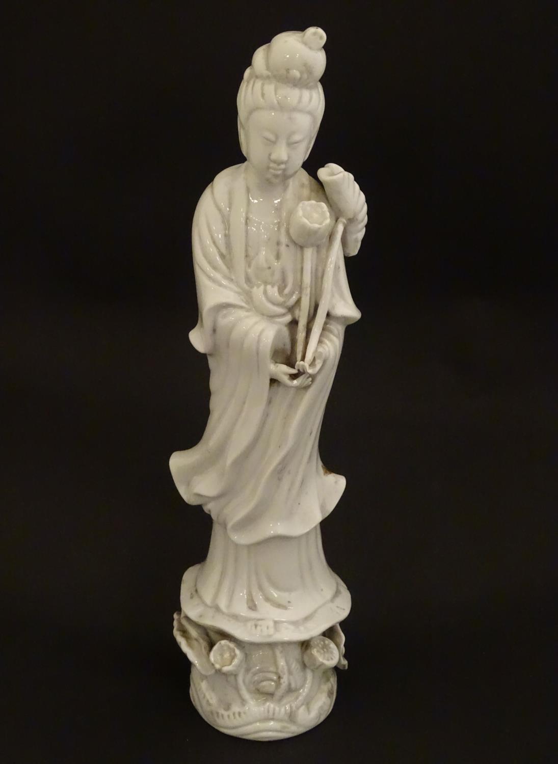 A Chinese blanc de chine figure of Guanyin holding flowers, raised on a base of lotus flowers and