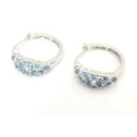 A pair of silver and white metal hoop earrings set with five graduated light blue stones. Stamped