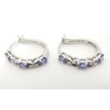 A pair of silver and white metal elongated hoop-like earrings set with three mauve stones. Stamped