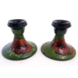 A pair of Moorcroft green ground squat candlesticks decorated with poppy flowers. Impressed marks to