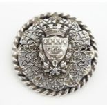 A white metal brooch of circular form with shield armorial to centre depicting Nordic long boat.