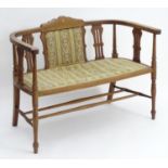 An Edwardian conversation sofa with upholstered seat and backrest with vase shaped pierced supports,