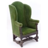 An 18thC wing back armchair with carved legs united by a turned H stretcher. 45" high x 26" deep x